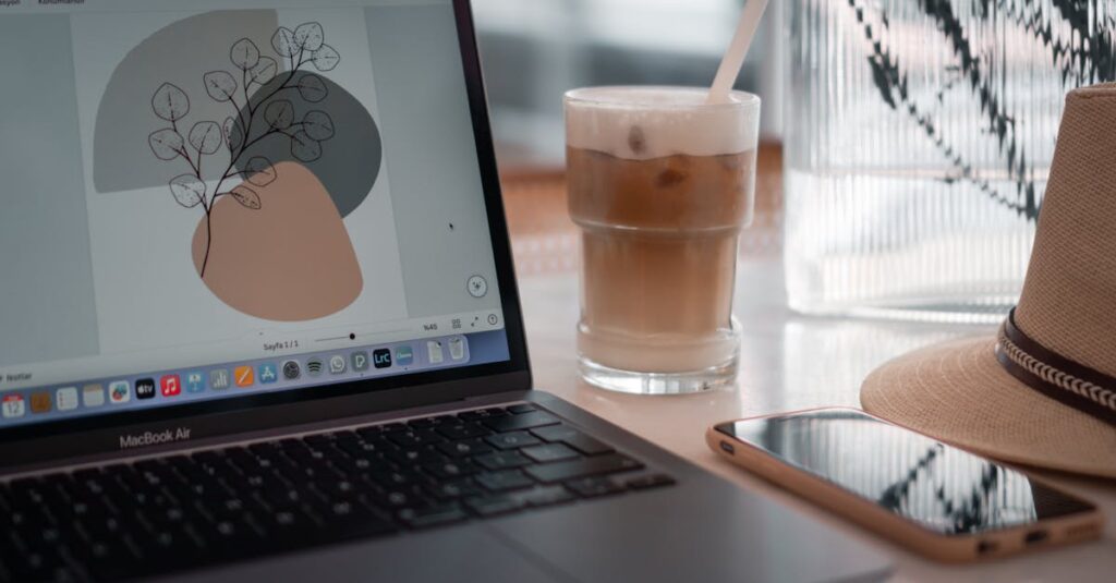 A modern workspace featuring a laptop, iced coffee, smartphone, and hat on a table.