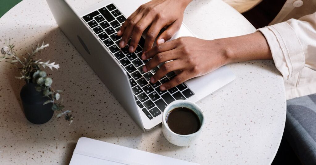 pexels photo 5052875 5052875 A person typing on a laptop at a café table with coffee and a notebook.